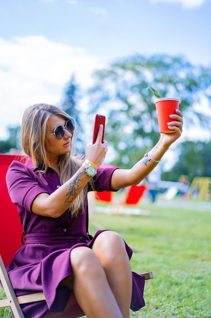 chica con un teléfono inteligente y un cóctel en la naturaleza en una tumbona. Día libre de verano.