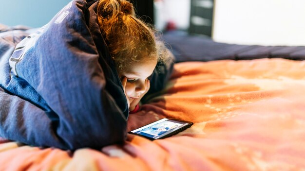 Chica con teléfono inteligente debajo de la manta