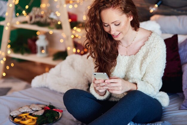 Chica con teléfono móvil pasar tiempo de Navidad en la cama