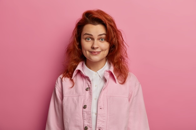 Una chica tierna de aspecto amistoso tiene el pelo rojo ondulado, sonríe con hoyuelos en las mejillas, se ve despreocupada y relajada, segura de sí misma, aislada sobre el espacio rosado. Gente