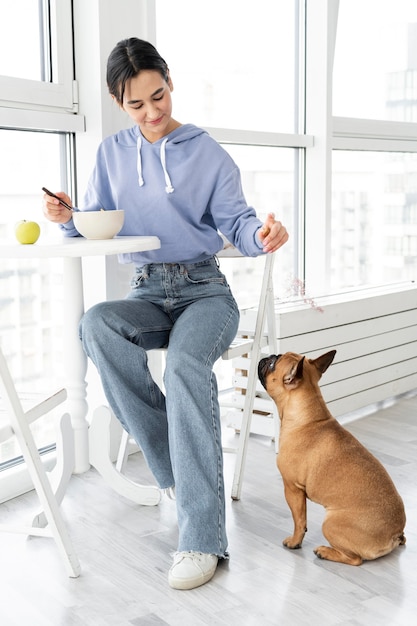 Chica de tiro completo comiendo cerca de perro