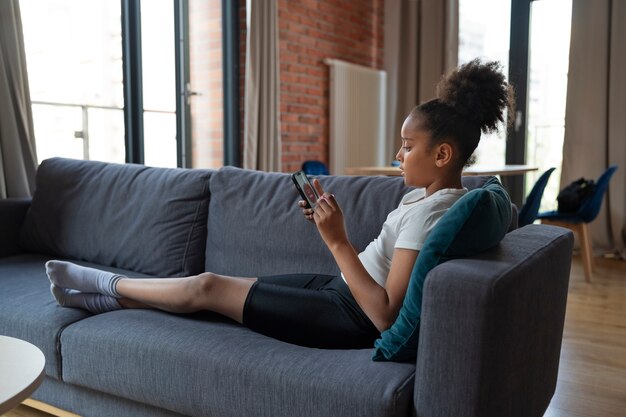 Chica de tiro completo en el sofá con teléfono inteligente