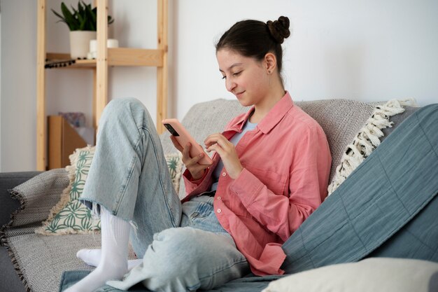 Chica de tiro completo en el sofá con teléfono inteligente