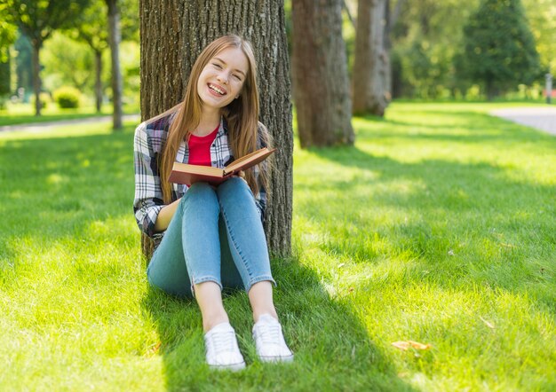 Chica de tiro largo leyendo afuera