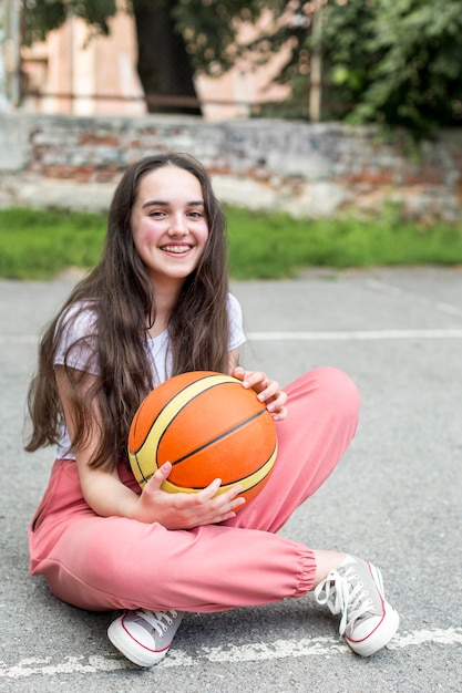 Chica de tiro largo sosteniendo una pelota de baloncesto al aire libre