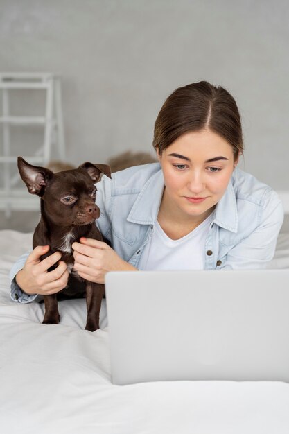 Chica de tiro medio en la cama con un portátil y un perro