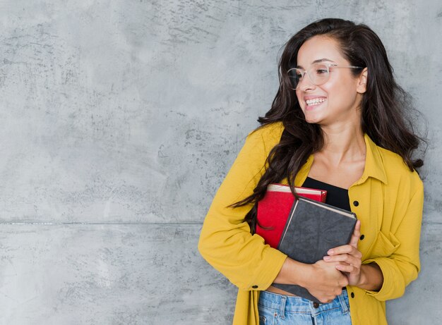 Chica de tiro medio con libros y fondo de cemento