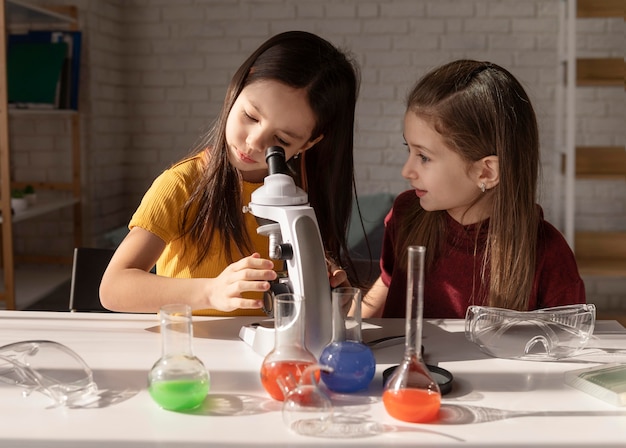 Chica de tiro medio mirando a través del microscopio