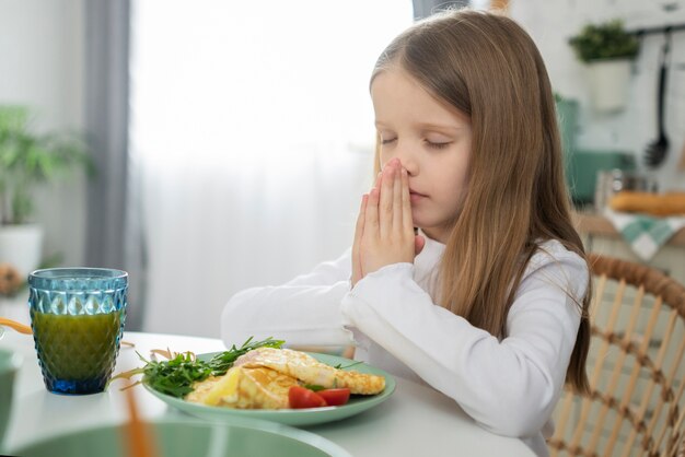 Chica de tiro medio rezando antes de comer