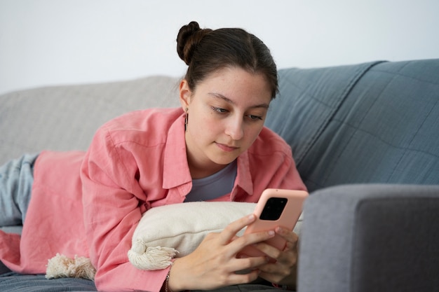 Chica de tiro medio en el sofá con teléfono inteligente