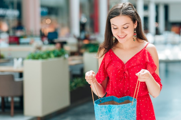 Chica de tiro medio sonriendo y sosteniendo una bolsa de compras