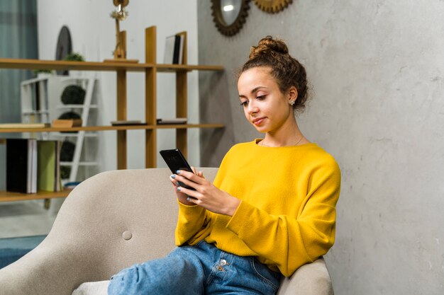 Chica de tiro medio con suéter amarillo y teléfono inteligente