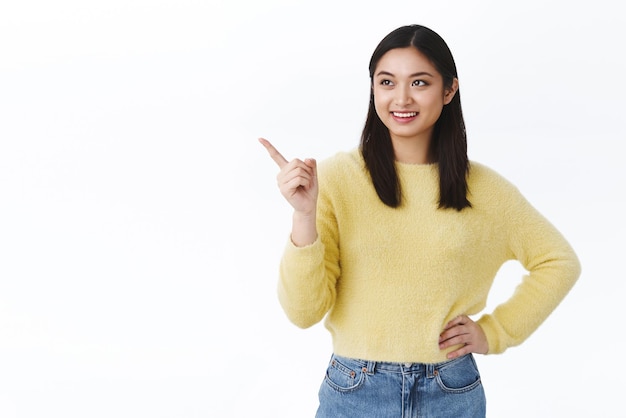 Chica toma la decisión de elegir el producto apuntando con el dedo en la esquina superior izquierda y sonriendo satisfecha con una buena elección de compras en el centro comercial recomendando el sitio web tienda en línea de fondo blanco