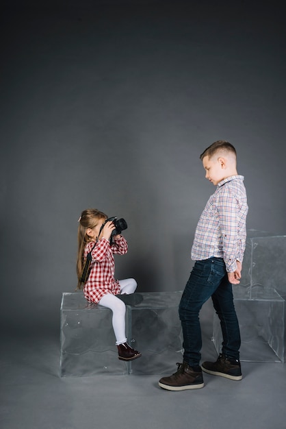 Foto gratuita chica tomando foto de un niño con cámara contra el fondo gris