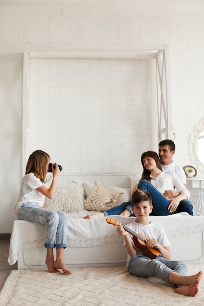 Foto gratuita chica tomando foto de sus padres y su hermano tocando el ukelele en casa