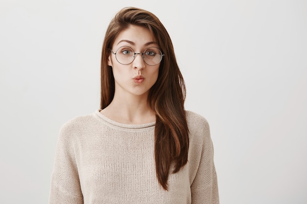 Chica tonta sorprendida haciendo pucheros, usando anteojos recetados de moda