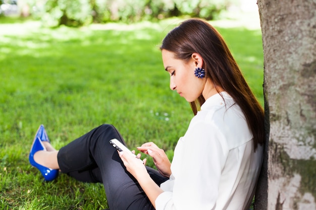 Chica trabaja con su teléfono sentado bajo el árbol