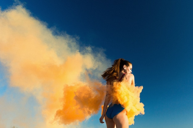 Foto gratuita chica en traje de baño azul baila con humo naranja en la playa blanca