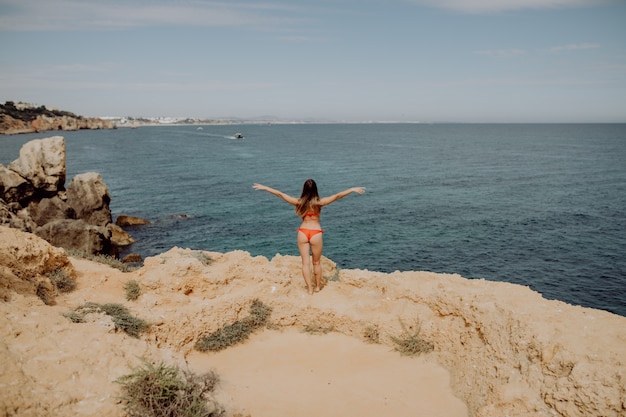 Chica en traje de baño rojo, con los brazos levantados posando en la playa