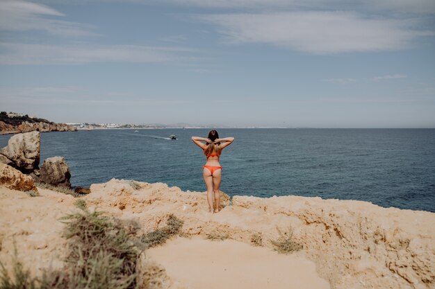 Chica en traje de baño rojo, con los brazos levantados posando en la playa