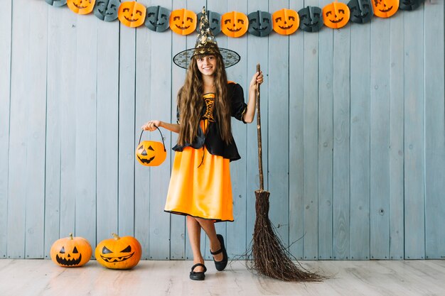 Chica en traje de bruja con cesta de Halloween y escoba