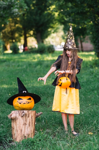 Chica en traje de bruja mostrando llegar manos en calabaza