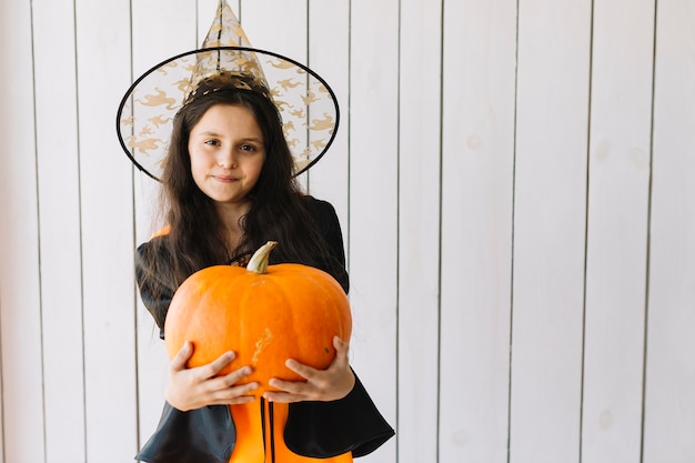 Chica en traje de Halloween con calabaza posando en estudio