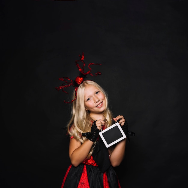 Chica en traje de Halloween que muestra la pizarra