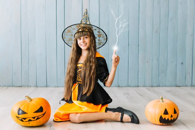 Chica en traje de Halloween sentado en el suelo y conjurar