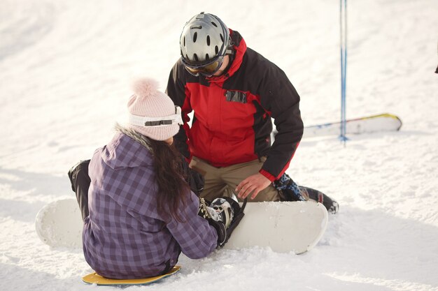 Chica tratando de subirse a una tabla de snowboard. Guy le da una mano a la chica. Traje morado.