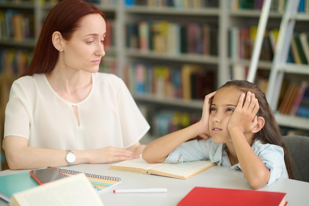 Chica triste y mujer joven estudiando en la mesa