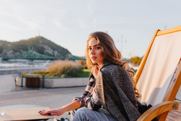 Chica triste con peinado elegante sentado en un café al aire libre en el fondo de la naturaleza