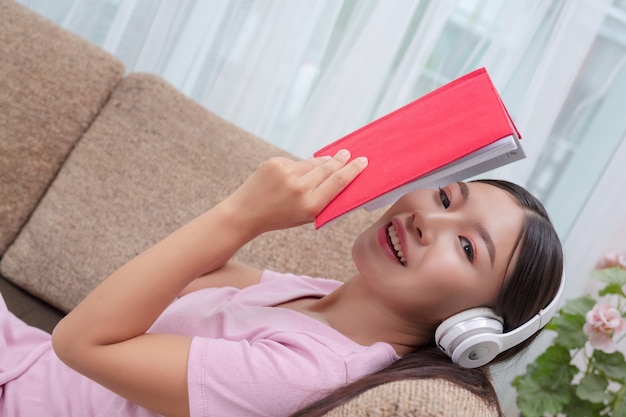 Chica tumbada en el sofá escuchando música y leyendo libros.