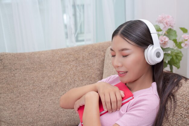 Chica tumbada en el sofá escuchando música y leyendo libros.