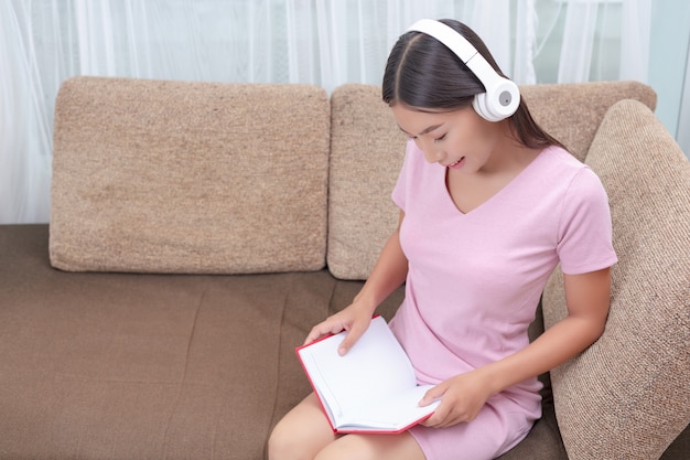 Chica tumbada en el sofá escuchando música y leyendo libros.