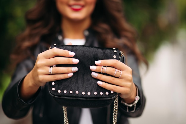 Chica con uñas cuidadas con hermoso adorno en anillos de boda sosteniendo una bolsa de piel negra.