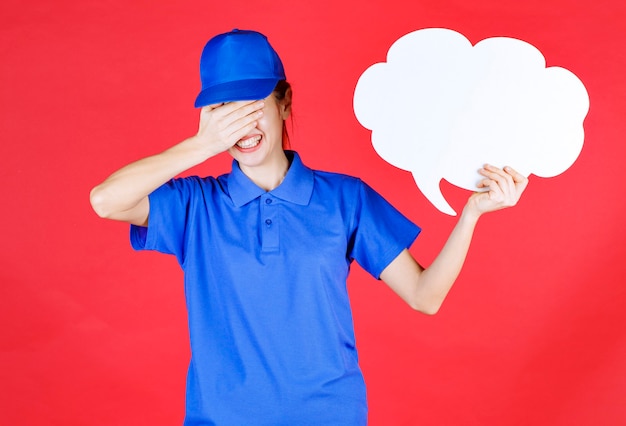 Chica en uniforme azul y boina sosteniendo un panel de ideas en forma de nube y parece cansada y tiene dolor de cabeza.