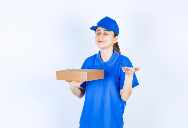 Chica en uniforme azul sosteniendo una caja de cartón para llevar y oliendo la comida.