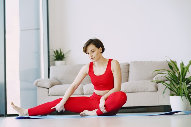 Chica en uniforme deportivo rojo practicando yoga en casa