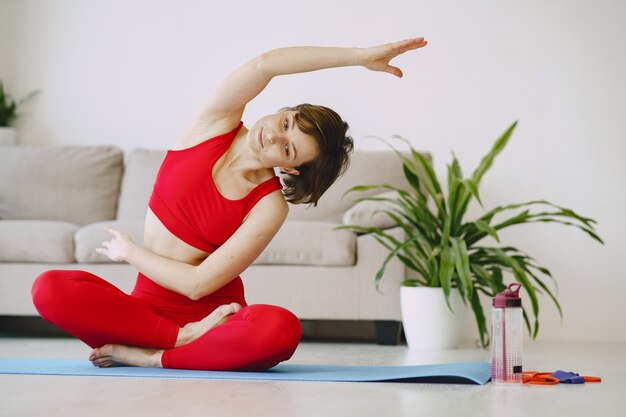 Chica en uniforme deportivo rojo practicando yoga en casa