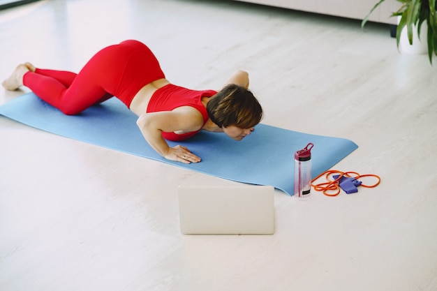 Chica en uniforme deportivo rojo practicando yoga en casa