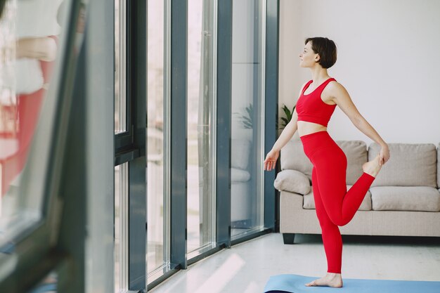 Chica en uniforme deportivo rojo practicando yoga en casa