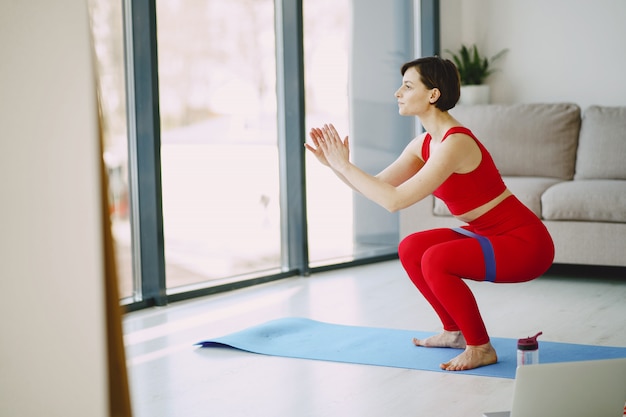 Chica en uniforme deportivo rojo practicando yoga en casa