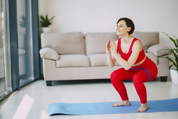 Chica en uniforme deportivo rojo practicando yoga en casa