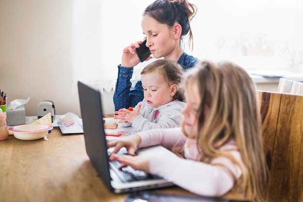 Chica usando la computadora portátil al lado de su madre hablando por teléfono inteligente