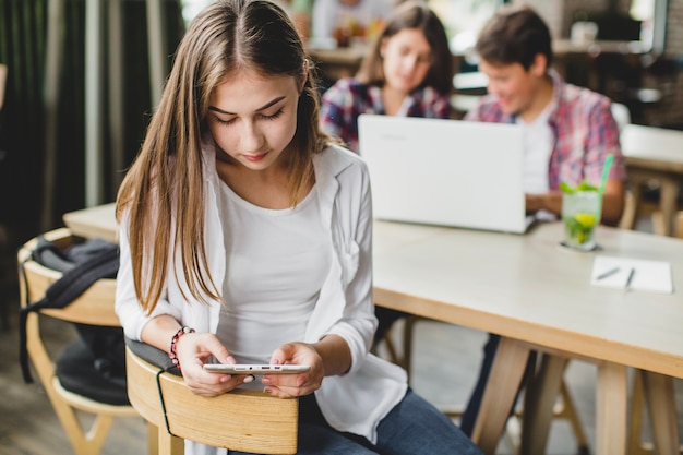 Chica usando tableta en el café con compañeros de clase