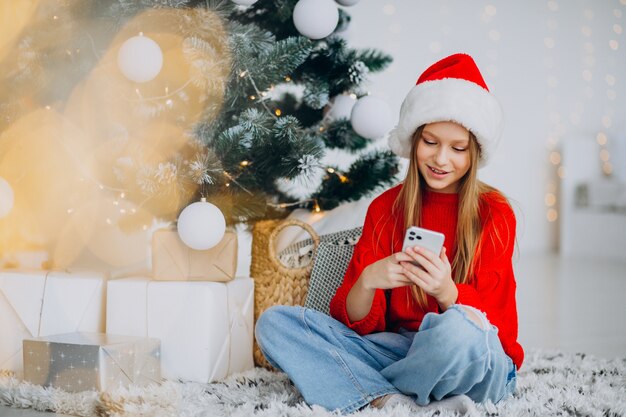 Chica usando el teléfono por el árbol de navidad en navidad