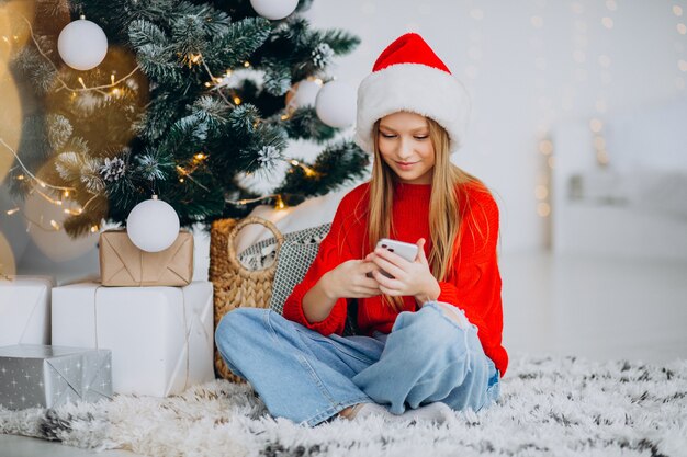 Chica usando el teléfono por el árbol de navidad en navidad