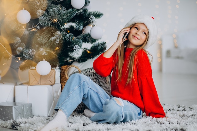 Chica usando el teléfono por el árbol de navidad en navidad