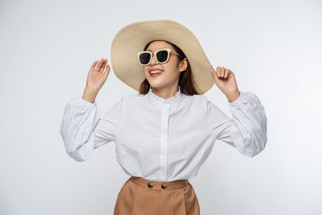 Chica vestida con una camisa blanca y pantalones cortos con sombrero Usar gafas y manejar el sombrero